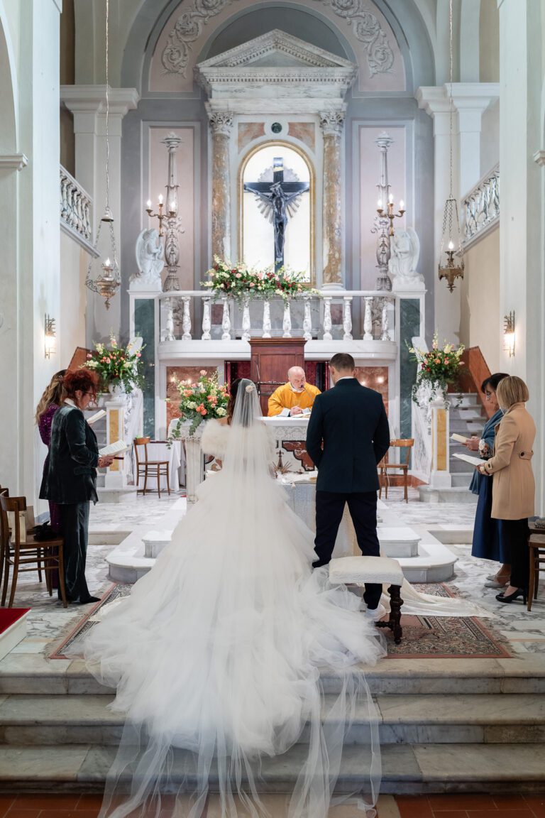 Una sposa e uno sposo stanno davanti a un altare dove un prete sta conducendo una cerimonia in un interno della chiesa splendidamente decorato, con gli ospiti che guardano, catturati in una splendida fotografia.