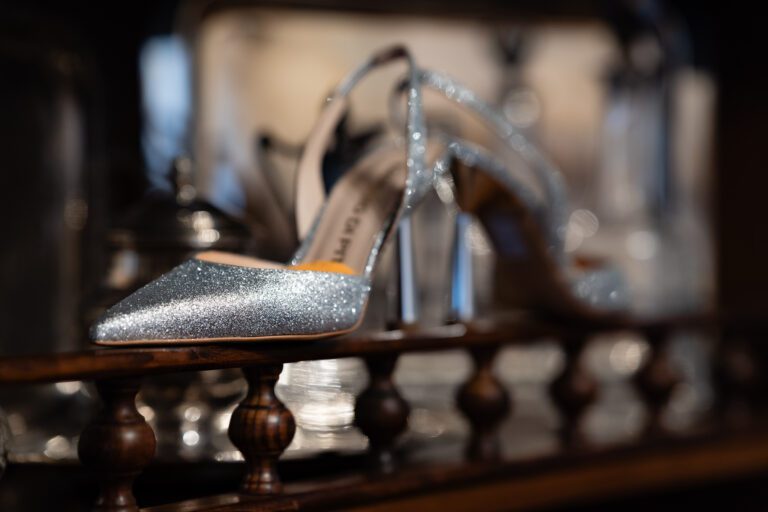 Un paio di scarpe argentate scintillanti con tacco alto posizionate su uno scaffale di legno, con uno sfondo sfumato che mette in risalto la struttura scintillante delle scarpe.