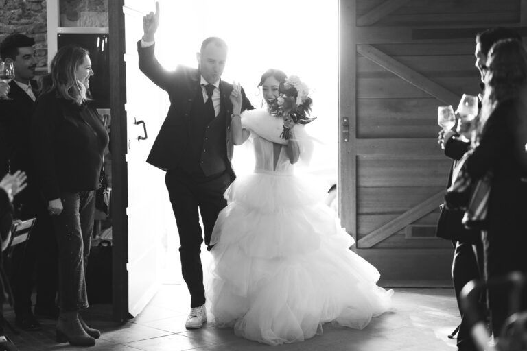 Una sposa e uno sposo gioiosi che ballano durante il ricevimento di nozze, circondati da ospiti applaudinti, catturati in una foto di matrimonio in bianco e nero.
