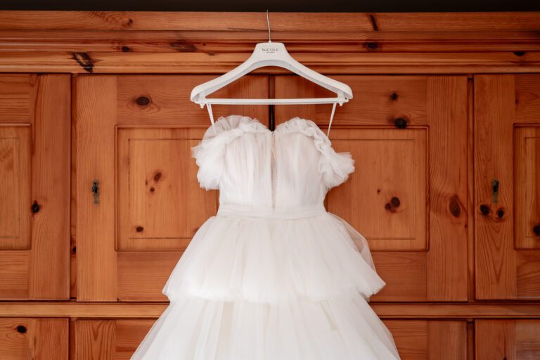 Un bellissimo abito da sposa bianco con strati di volant appeso a una gruccia con l'etichetta "sposa", sullo sfondo di un mobiletto rustico in legno in una foto di matrimonio.